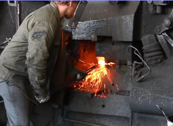 A Warwood Tool forge worker shaping heated steel beneath a forging hammer