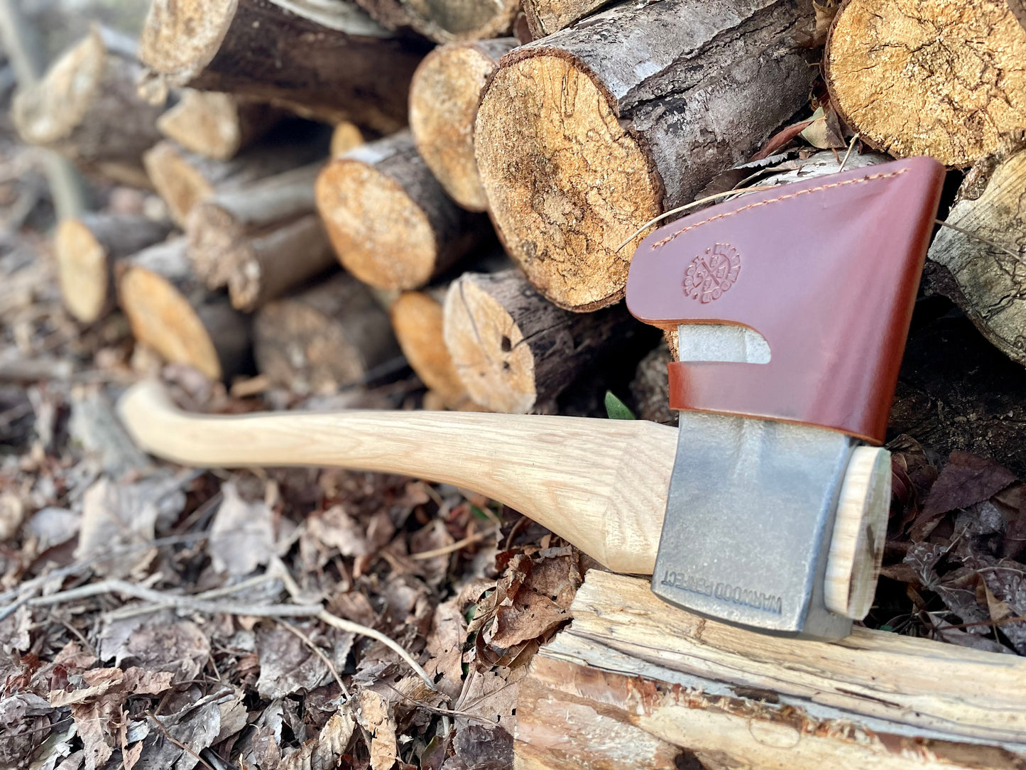 Warwood Tool's Perfect Axe with sheath on, laid next to a log pile.